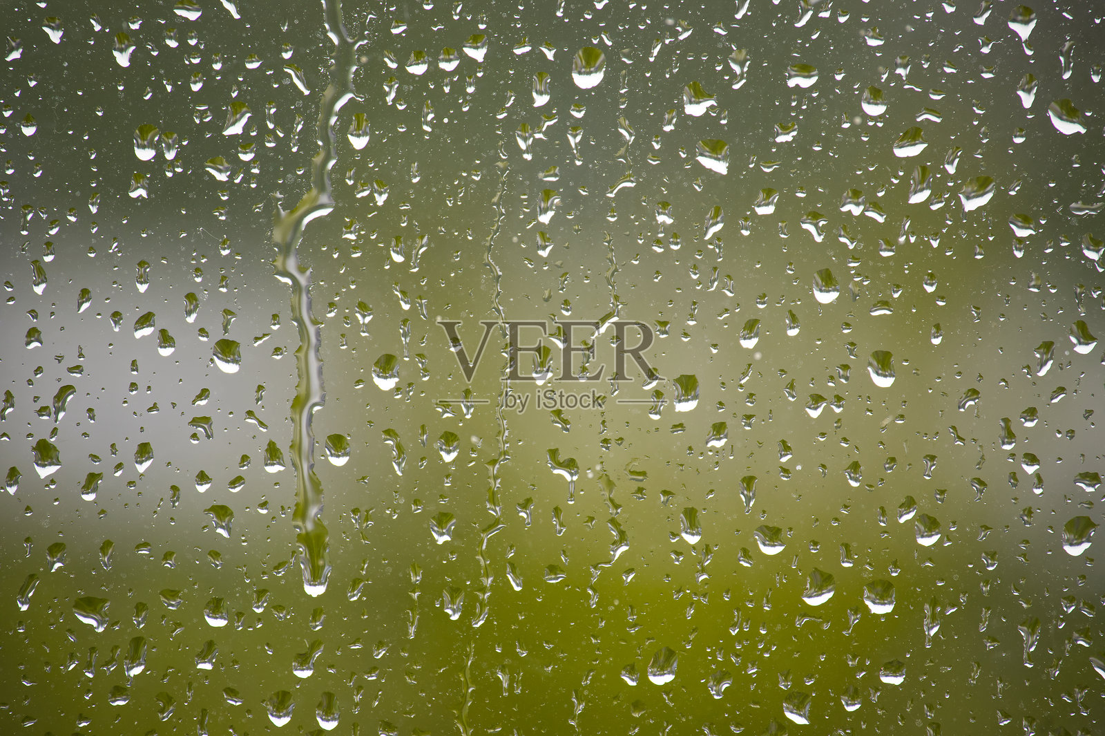 雨滴沿着窗户倾泻而下,形成一个宁静的景象,背景是一片模糊的绿色。照片摄影图片