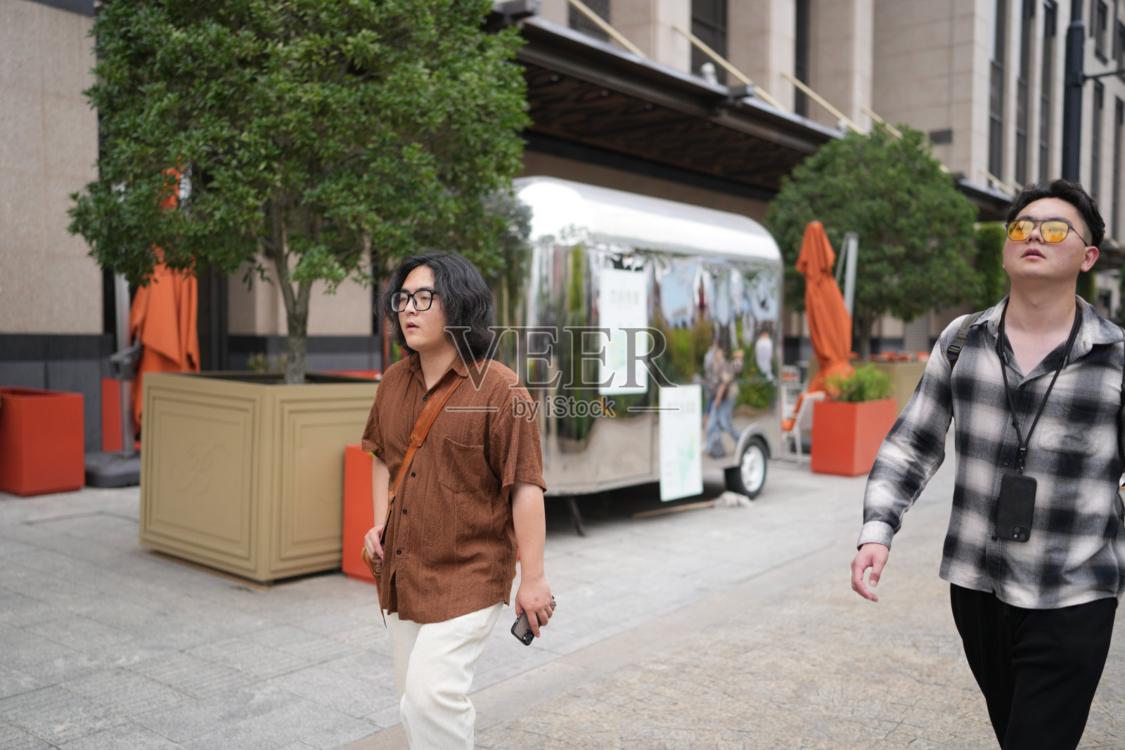 两位二十出头的年轻中国男子,佩戴眼镜,肩并肩走在繁忙的外滩主干道上,享受着2025年5月上海宜人的春季天气。照片摄影图片