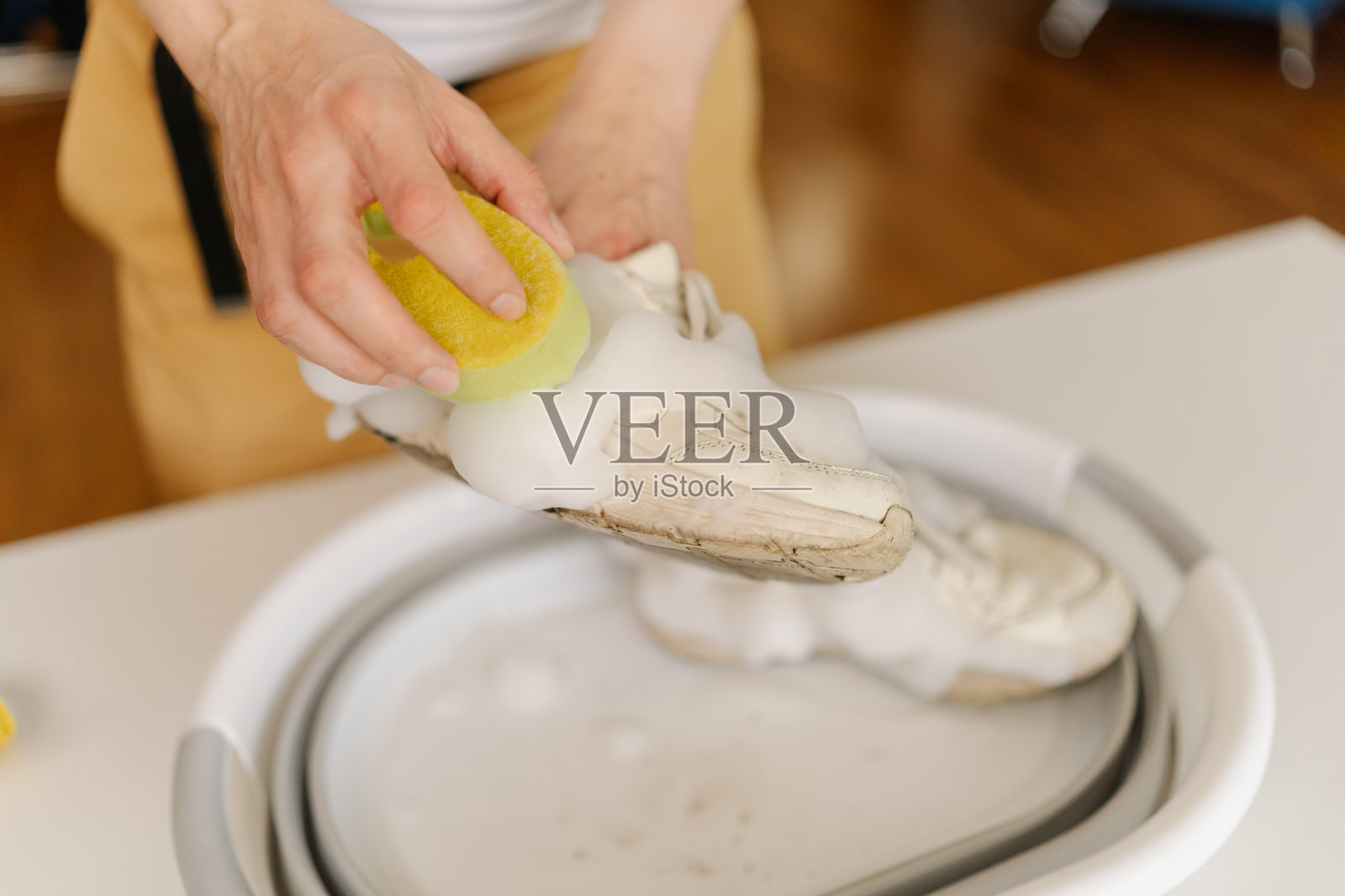 男人在家中用黄色海绵和肥皂在盆中清洗脏白色运动鞋,专注于去除污渍,保持鞋子干净清新,特写镜头。照片摄影图片