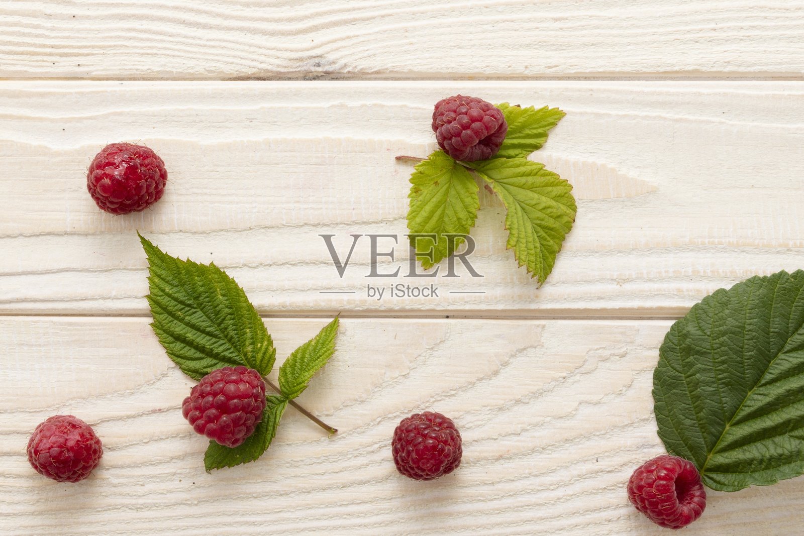 新鲜的覆盆子和绿色叶子在浅色木质背景上,俯视图照片摄影图片