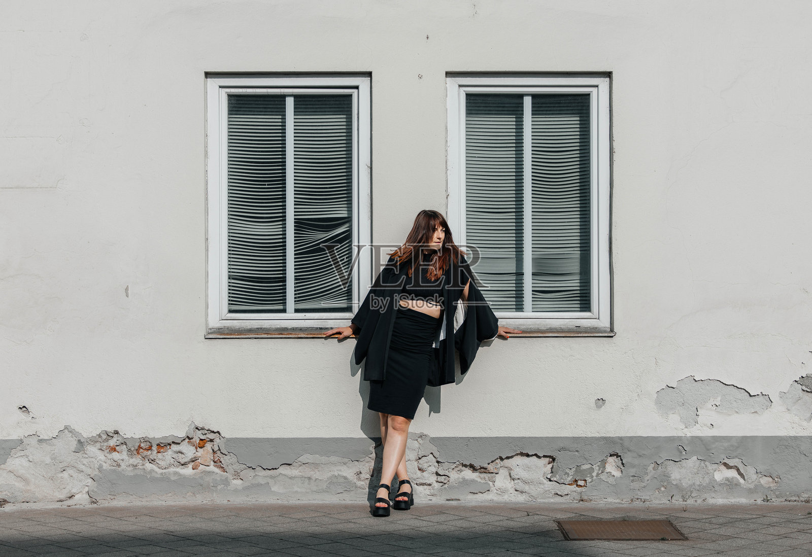 年轻的白人女性穿着黑色服装,站在白色墙壁前。照片摄影图片