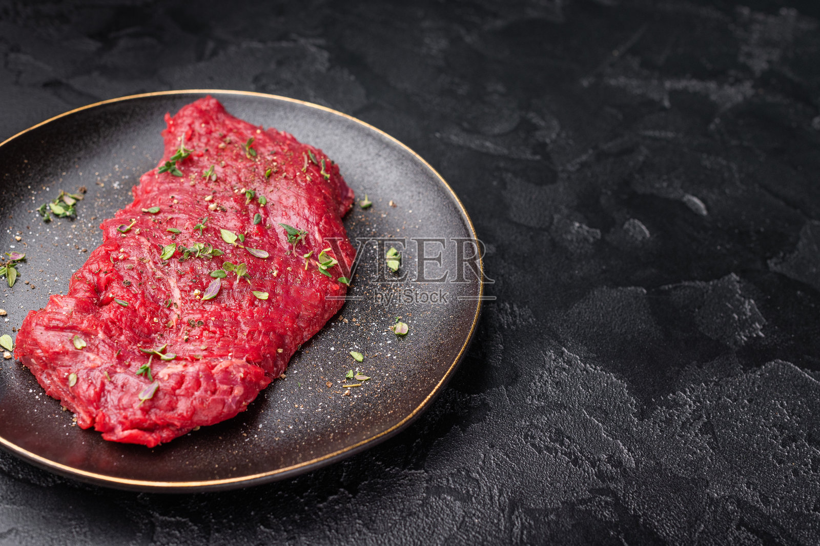 腌制的腹肉或牛腩生肉,配有百里香和香料,放在盘子里。黑色背景。俯视图。照片摄影图片