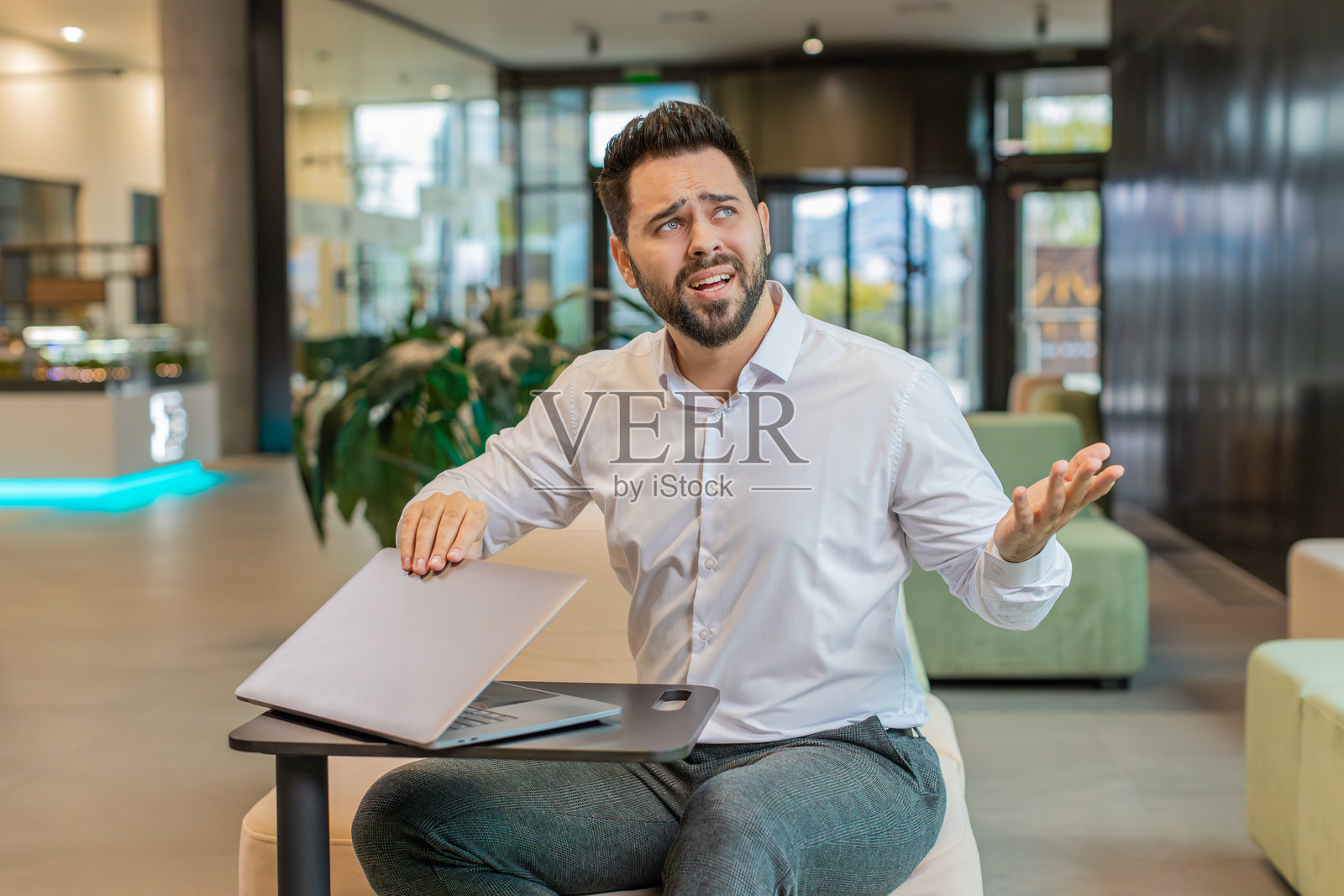 疲惫不堪的年轻白人男商人经理坐在现代办公室大堂里关闭笔记本电脑照片摄影图片