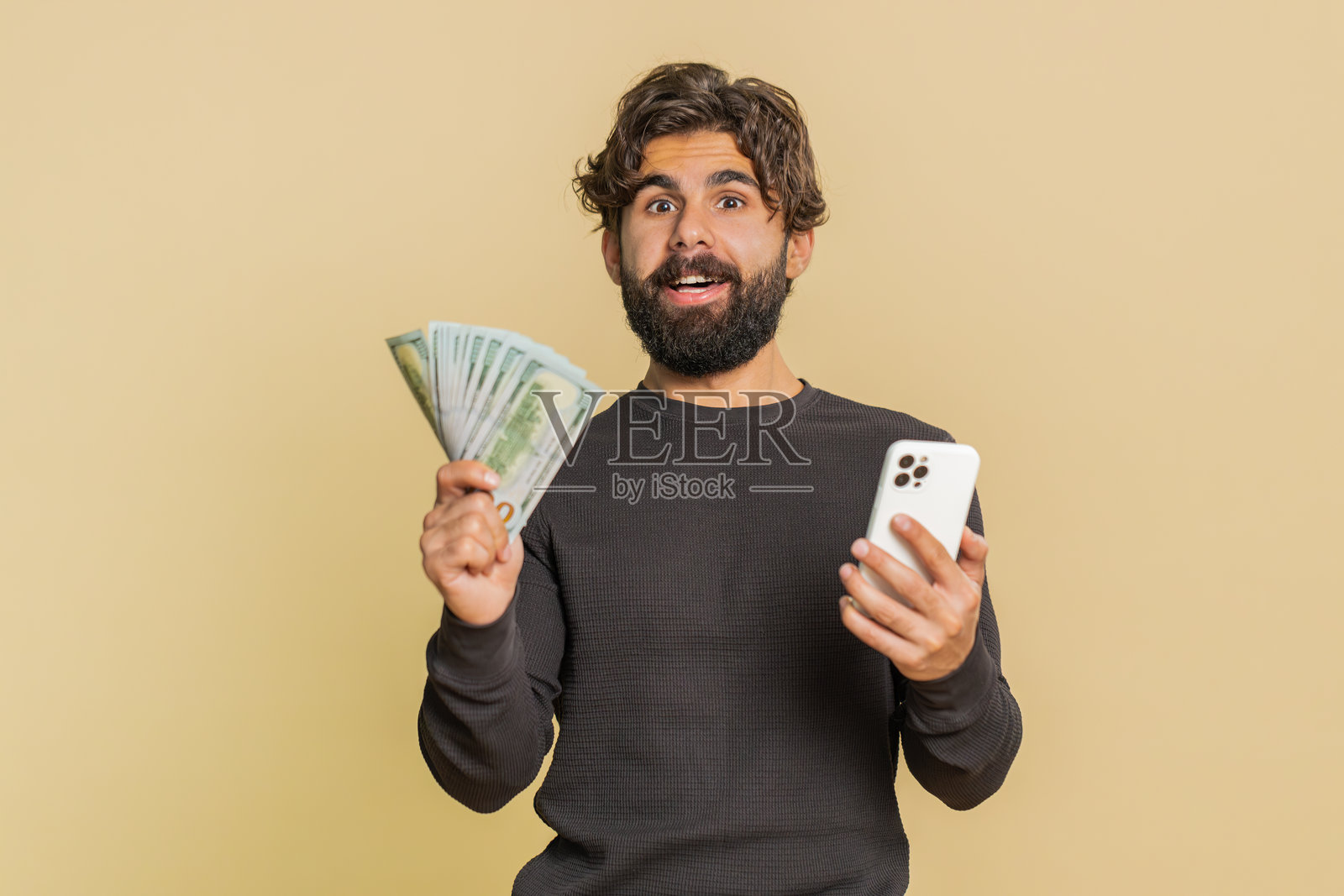 成功的黎巴嫩年轻人使用智能手机,手持钞票,背景为米色。照片摄影图片