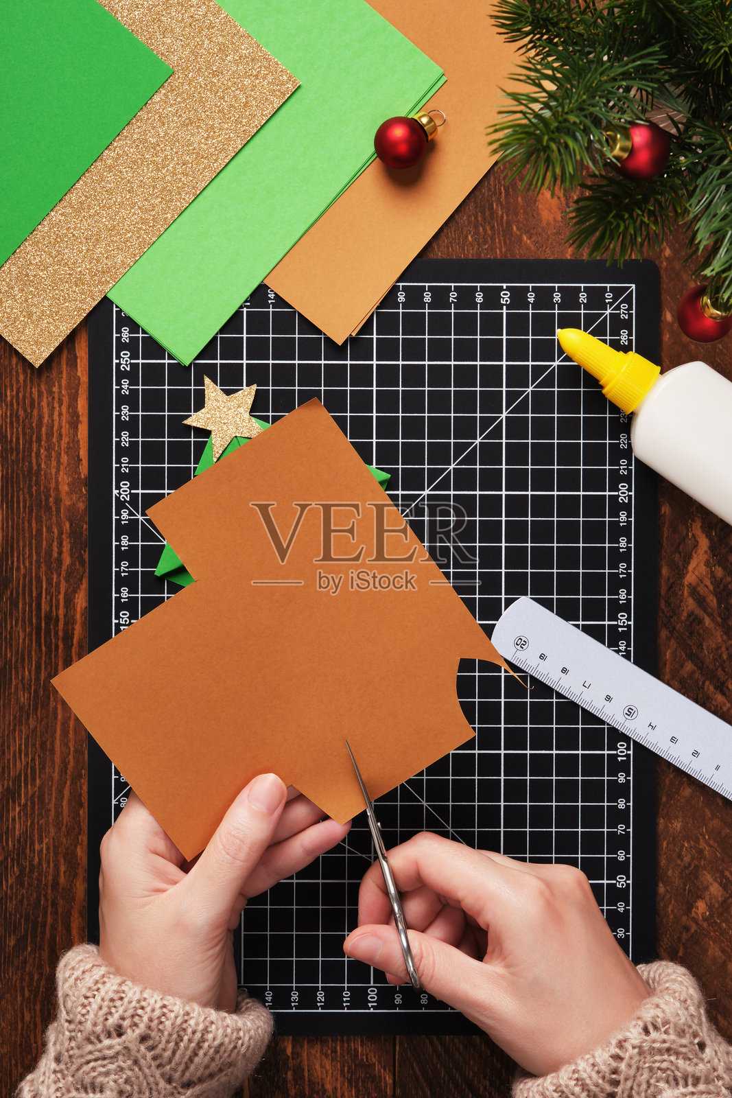 让我们做一个简单的纸艺。一个形状像圣诞树的书签。从棕色纸上剪下树干。照片摄影图片