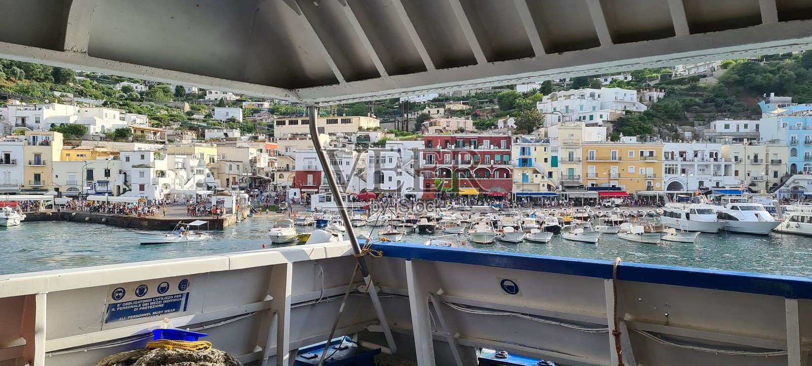 从船上俯瞰充满活力的意大利沿海小镇全景,五彩斑斓的建筑、繁忙的码头生活、山坡上的住宅,以及人们在热闹的海滨漫步。照片摄影图片