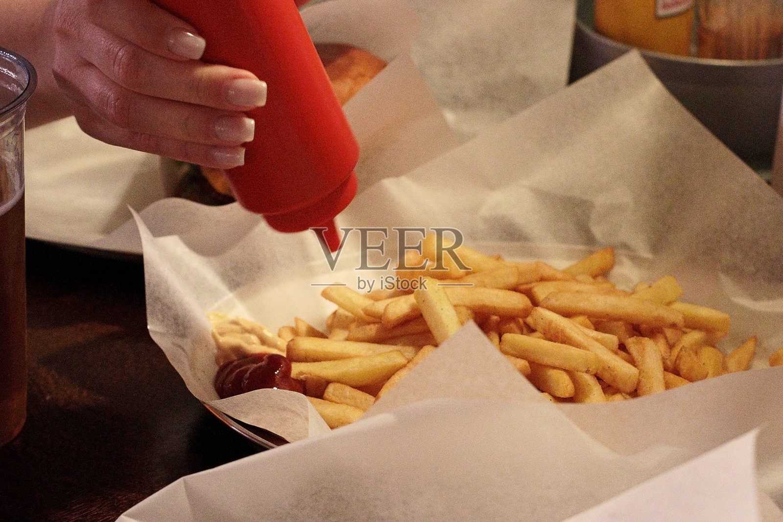 特写晚餐场景,手在纸托盘上的薯条上倒番茄酱。美味的快餐午餐,完美适合街头食品、小吃时间或休闲用餐生活方式概念。美国快餐照片摄影图片