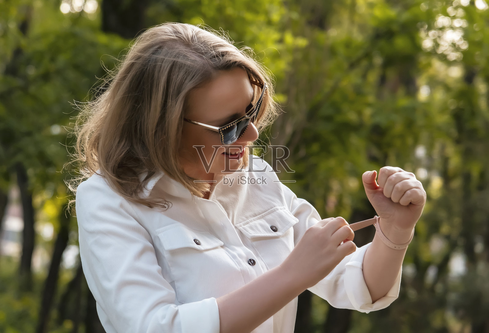 女人在公园里享受夏日散步,微笑着查看她的健身手环。照片摄影图片