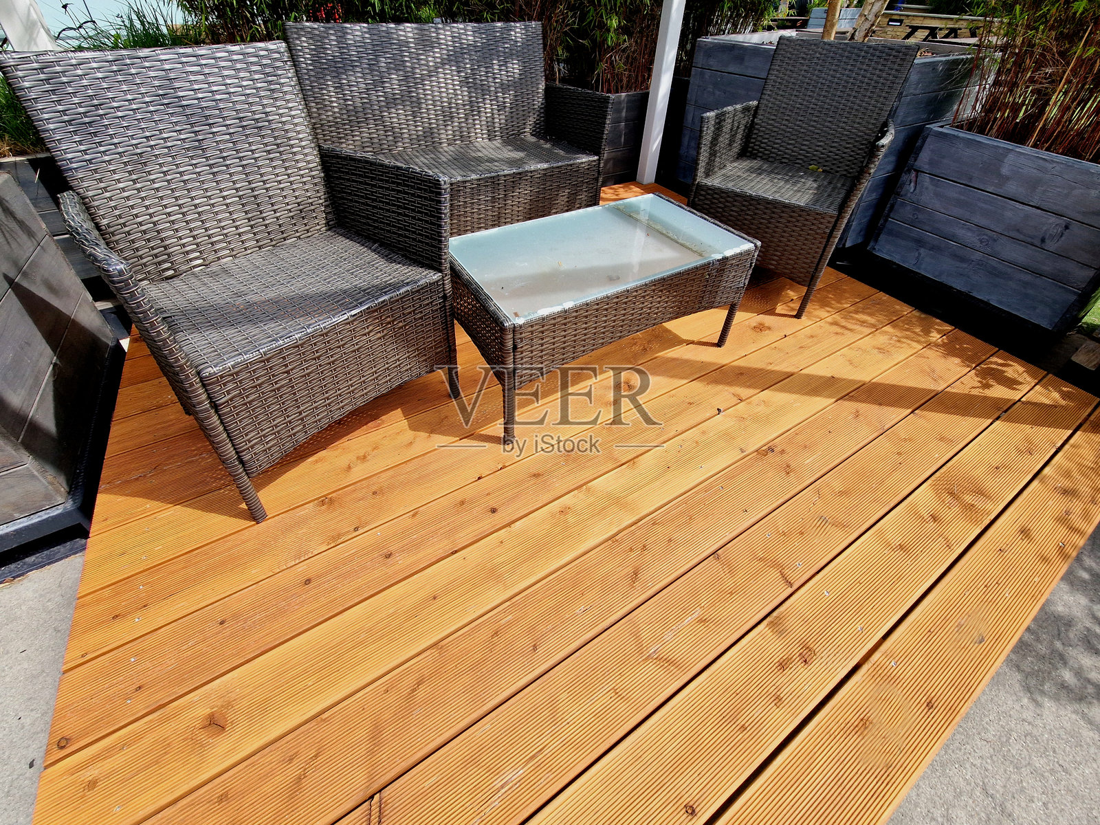 带有藤编外观椅子的露台。木质露台位于一个非正式风格的庭院花园中,花盆用灰色木板覆盖。照片摄影图片