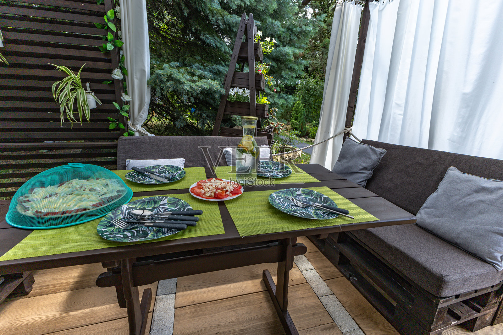花园凉亭下的木桌,准备在花园里享用晚餐,桌上摆放着盘子。照片摄影图片
