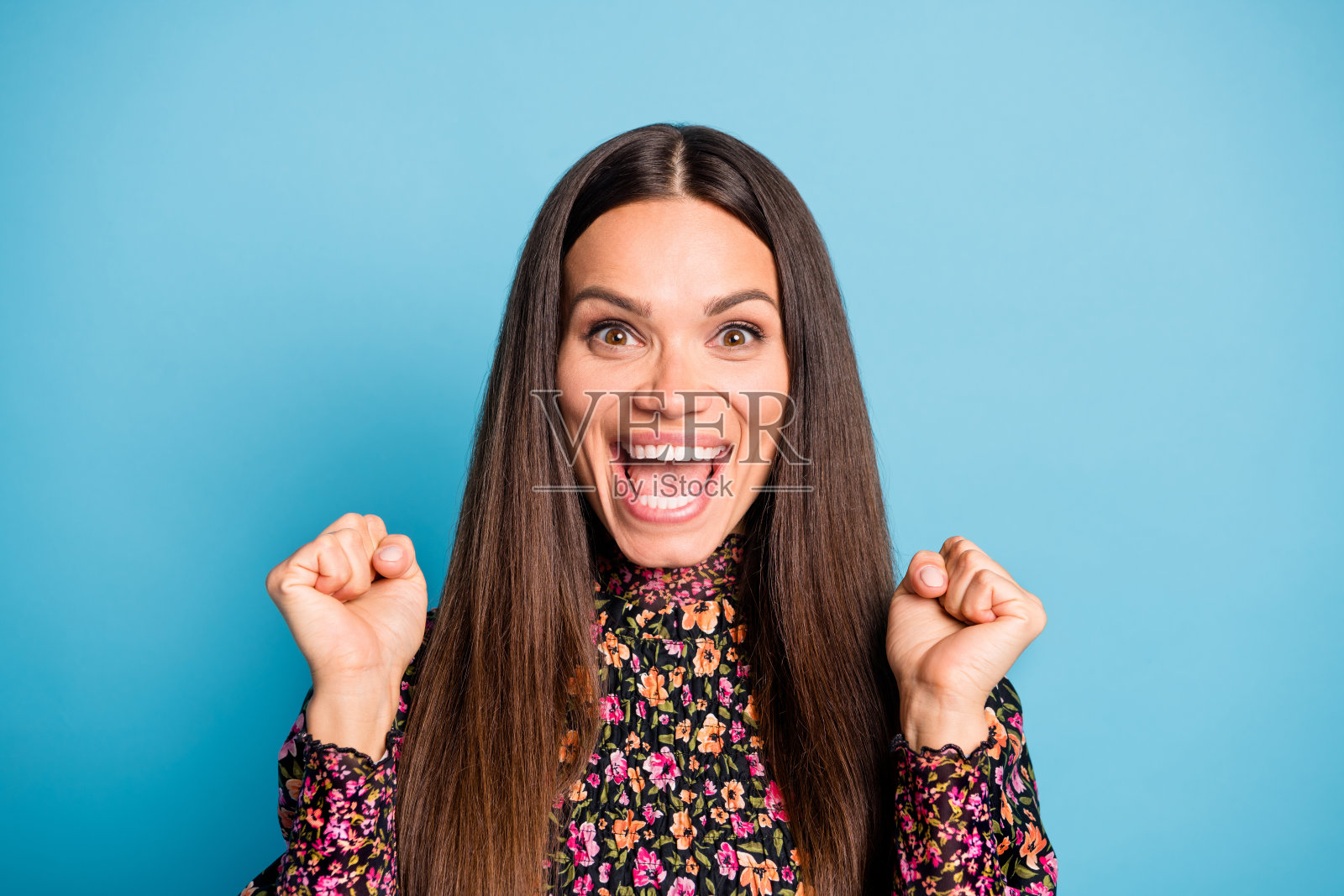 年轻快乐兴奋的女性微笑着,双拳握紧庆祝胜利,背景为蓝色。照片摄影图片