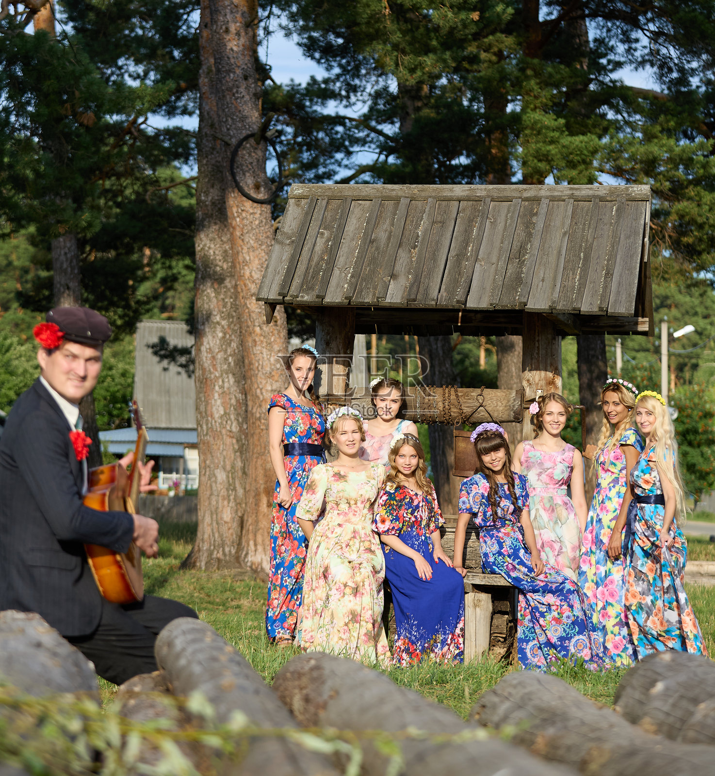 一位快乐的男性民谣音乐家在乡村的水井旁为一群年轻美丽的女性弹吉他照片摄影图片