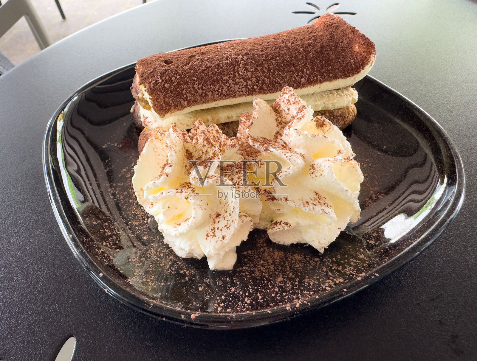 黑盘上的提拉米苏甜点,配有鲜奶油照片摄影图片