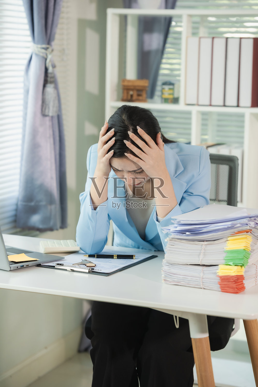 一位女性正在桌子上处理文件和档案。她在整理文件,审查财务信息。她一边审查重要文件,一边手里拿着一叠文件。照片摄影图片