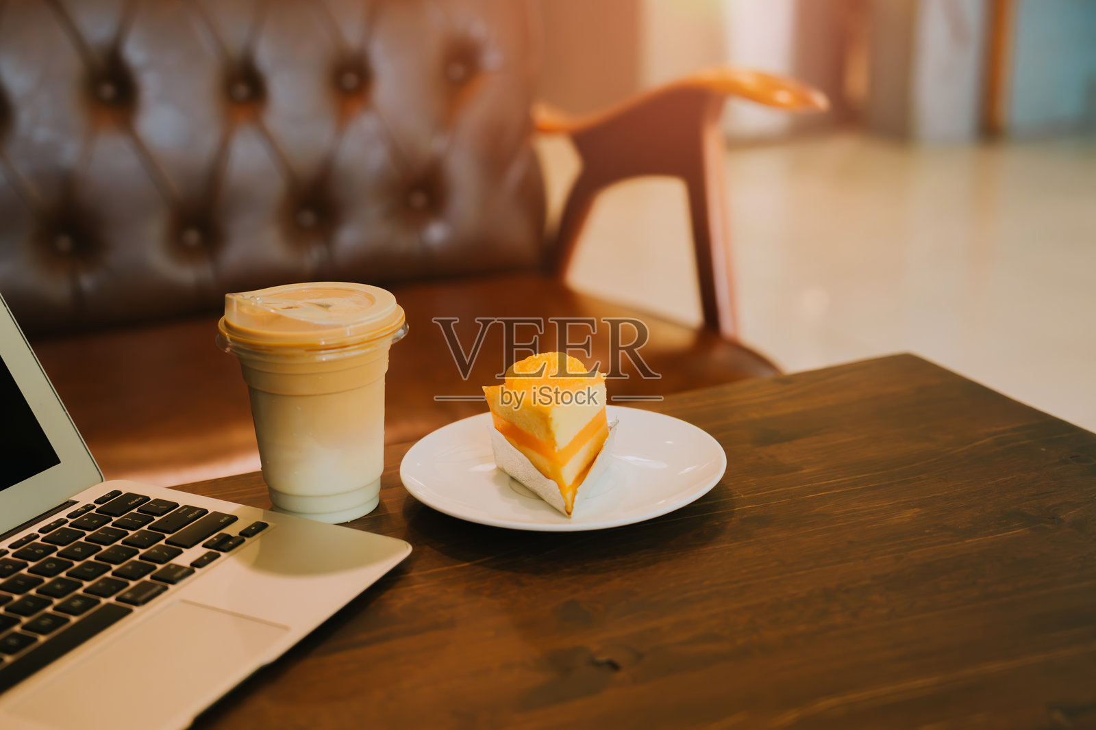 舒适的咖啡店环境,配有笔记本电脑、清爽饮品、明亮的蛋糕切片和舒适的扶手椅照片摄影图片