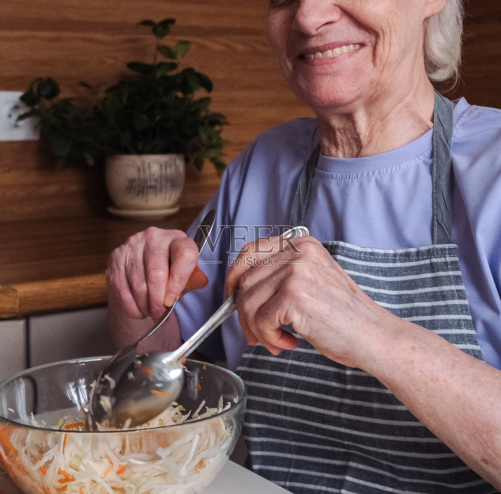 一位短发的老年女性坐在厨房台面前,正在搅拌新鲜的卷心菜和胡萝卜沙拉。照片摄影图片