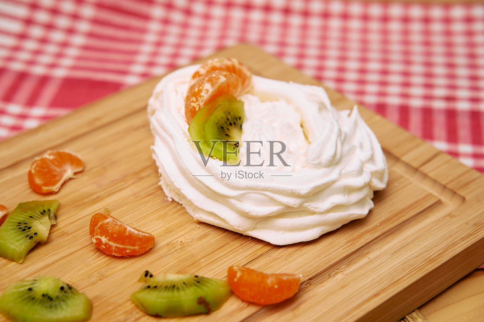 木板上的奇异果和橘子的蛋白霜甜点,背景为格子图案照片摄影图片