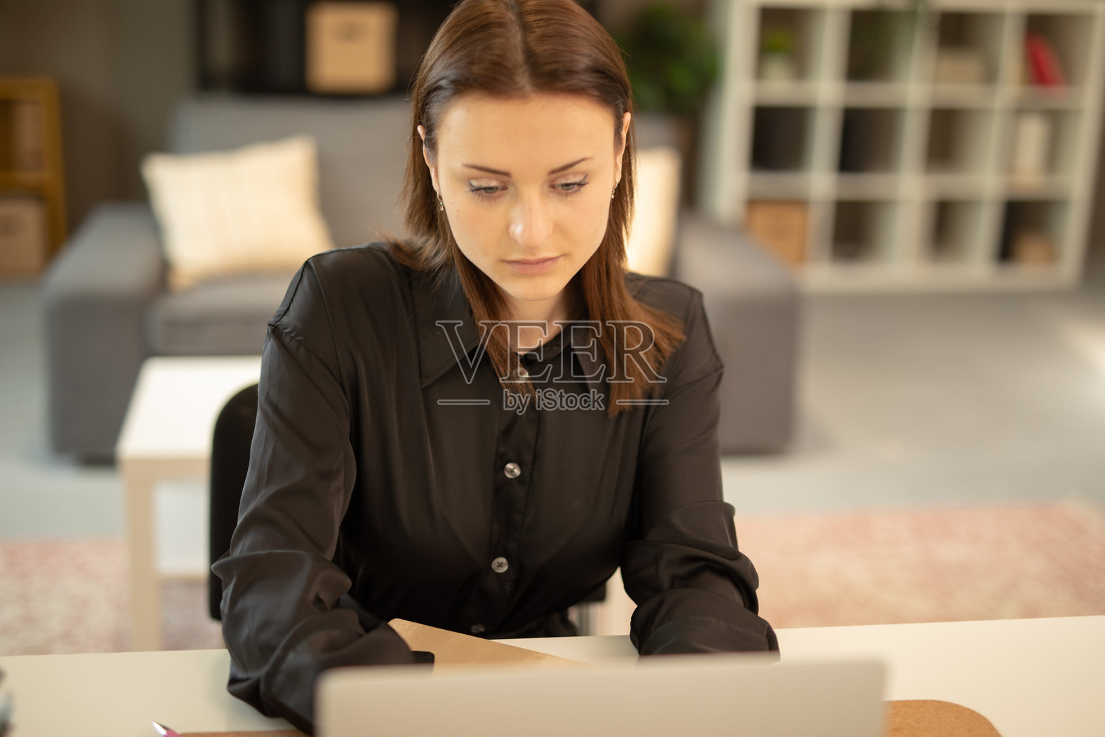 专注的年轻女性在家中办公室使用笔记本电脑工作。照片摄影图片