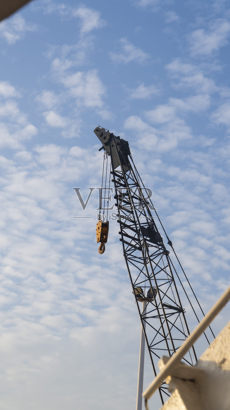 在明亮的蓝天和白云下,一只大型黑色起重机带着钩子。照片摄影图片