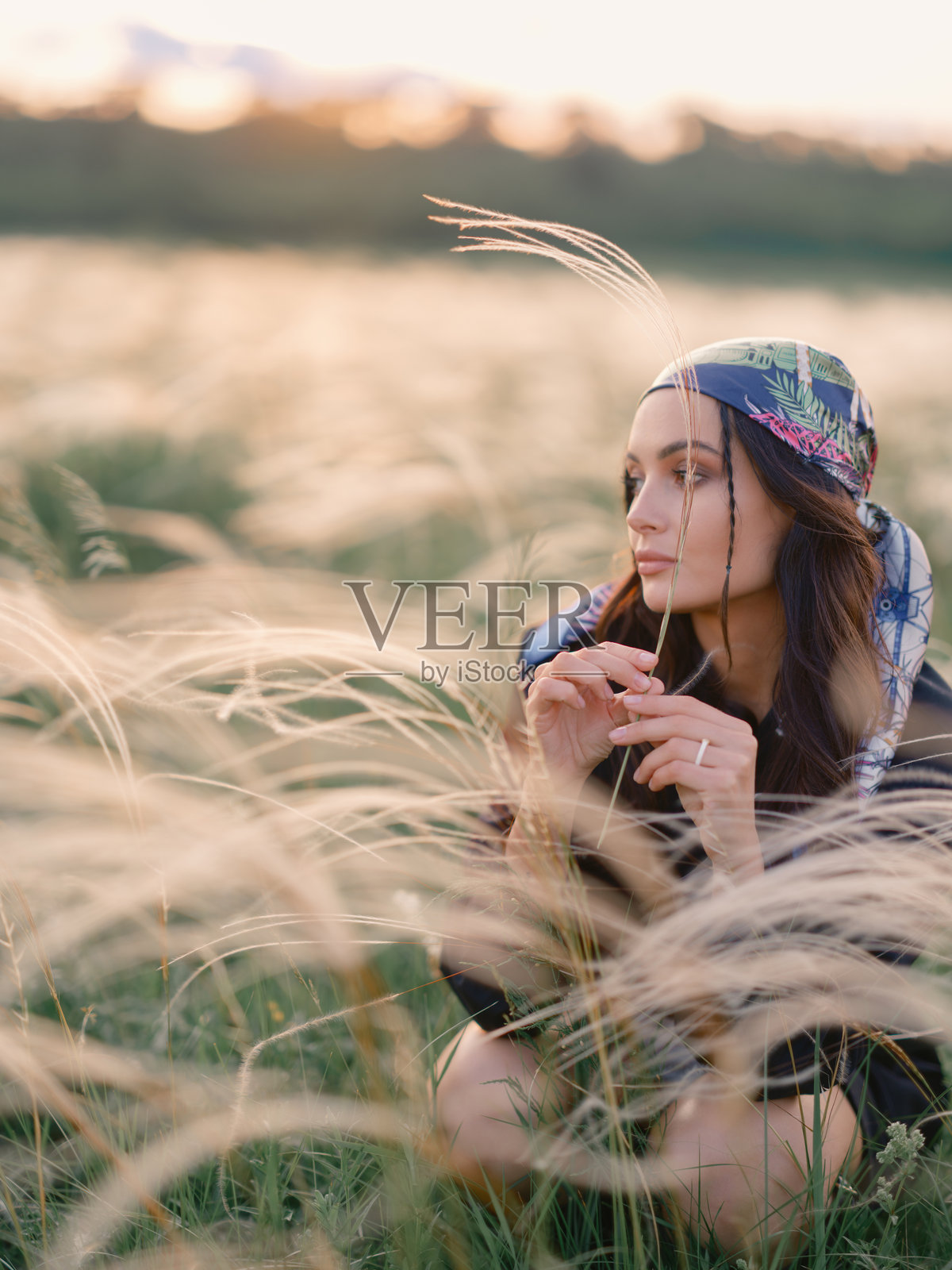 年轻女性坐在草原上的羽毛草中放松,夕阳下的美丽景色。照片摄影图片