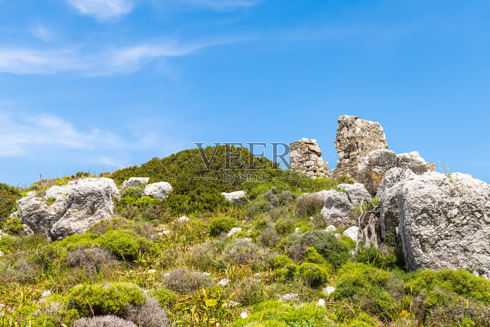在希腊伊卡里亚岛的德拉卡诺塔楼附近,徒步小径的山脚下堆叠着岩石和古老遗迹。照片摄影图片