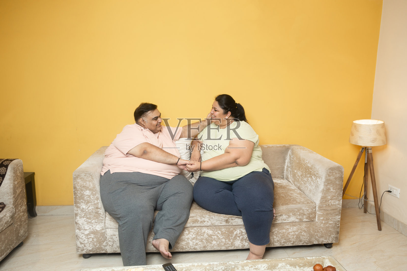快乐的印度胖夫妇坐在家里的沙发上。肥胖的丈夫和妻子手牵手放松。肥胖。爱与亲密。加大码男士和女士。照片摄影图片