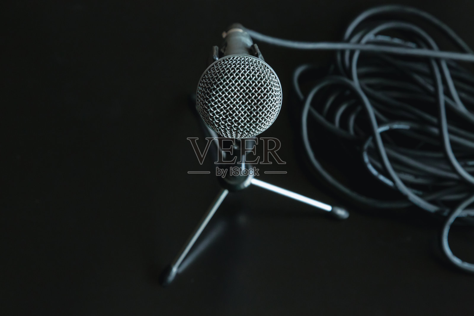 一个麦克风稳稳地放在黑色桌面上的特殊麦克风支架上,旁边是一条卷绕的黑色音频电缆,象征着言论自由、公众演讲和采访,播客和现场直播。照片摄影图片