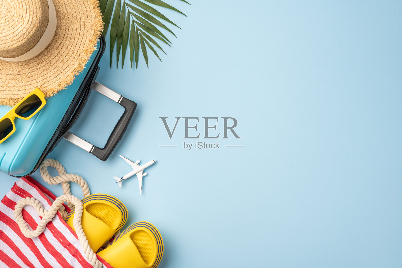 色彩缤纷的旅行物品整齐排列,包括蓝色行李箱、草帽、夏季鞋子、太阳镜和玩具飞机,体现了夏季假期的精神和探索的乐趣。照片摄影图片