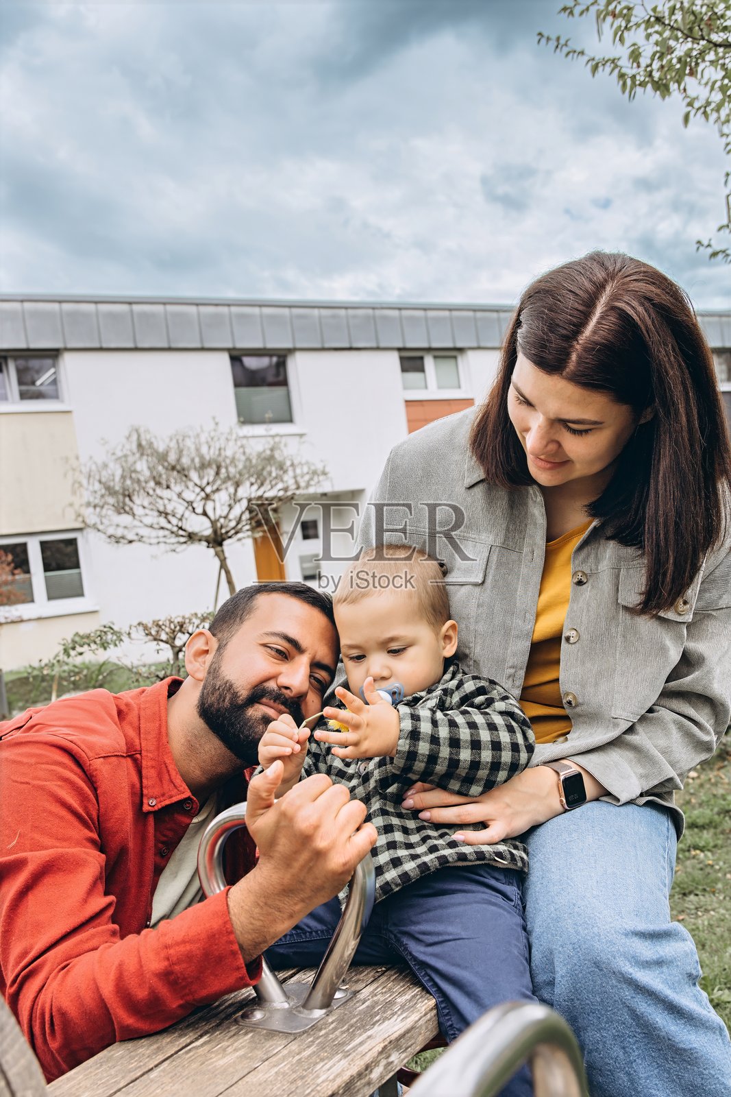 母亲、父亲和他们的小儿子在游乐场一起荡秋千的特写。家庭互动、育儿、亲密关系以及共享的童年经历在户外环境中。照片摄影图片