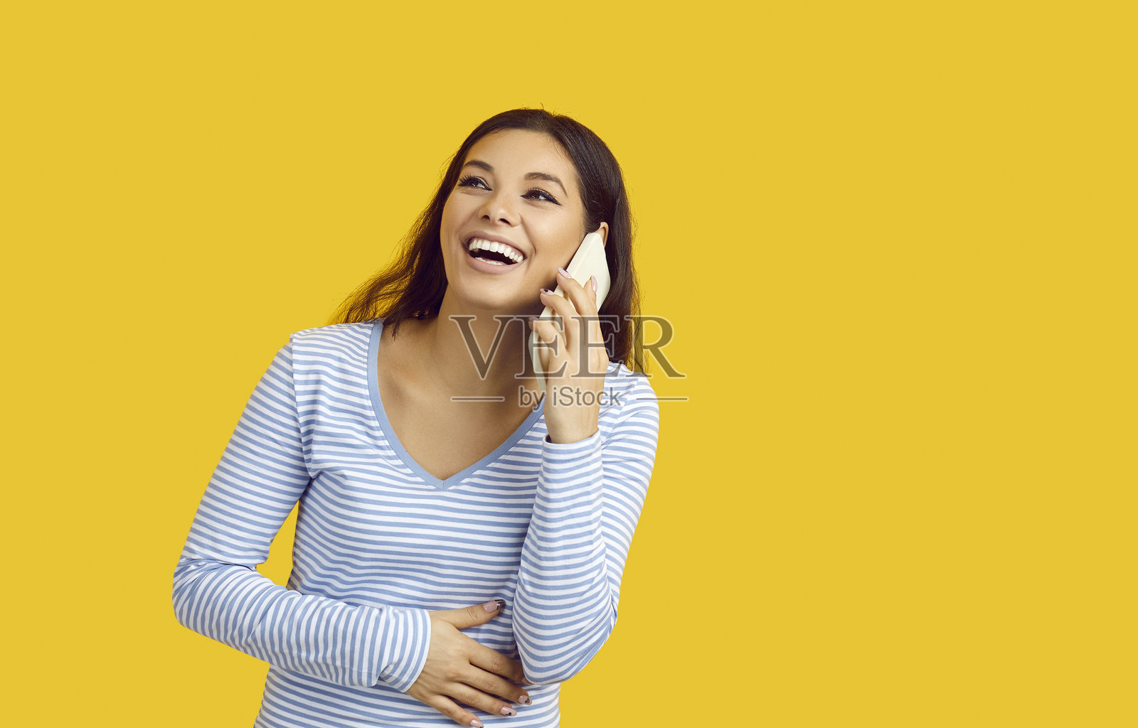 兴奋的女性用手触摸肚子,正在电话中交谈,背景为黄色,留有空白空间。照片摄影图片