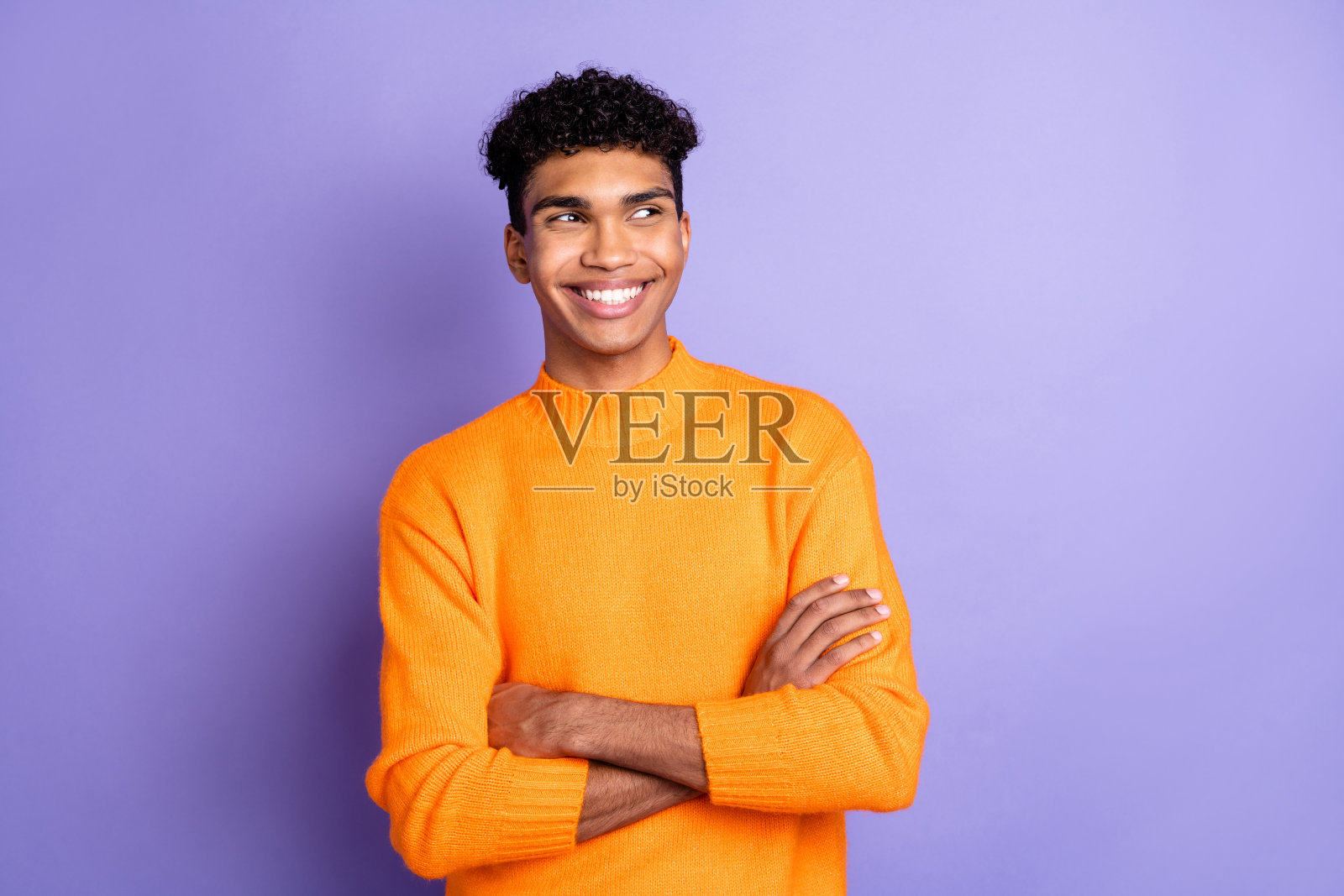 梦幻般的非裔美国年轻帅气男子自信地双手交叉,独自站在紫色背景前。照片摄影图片