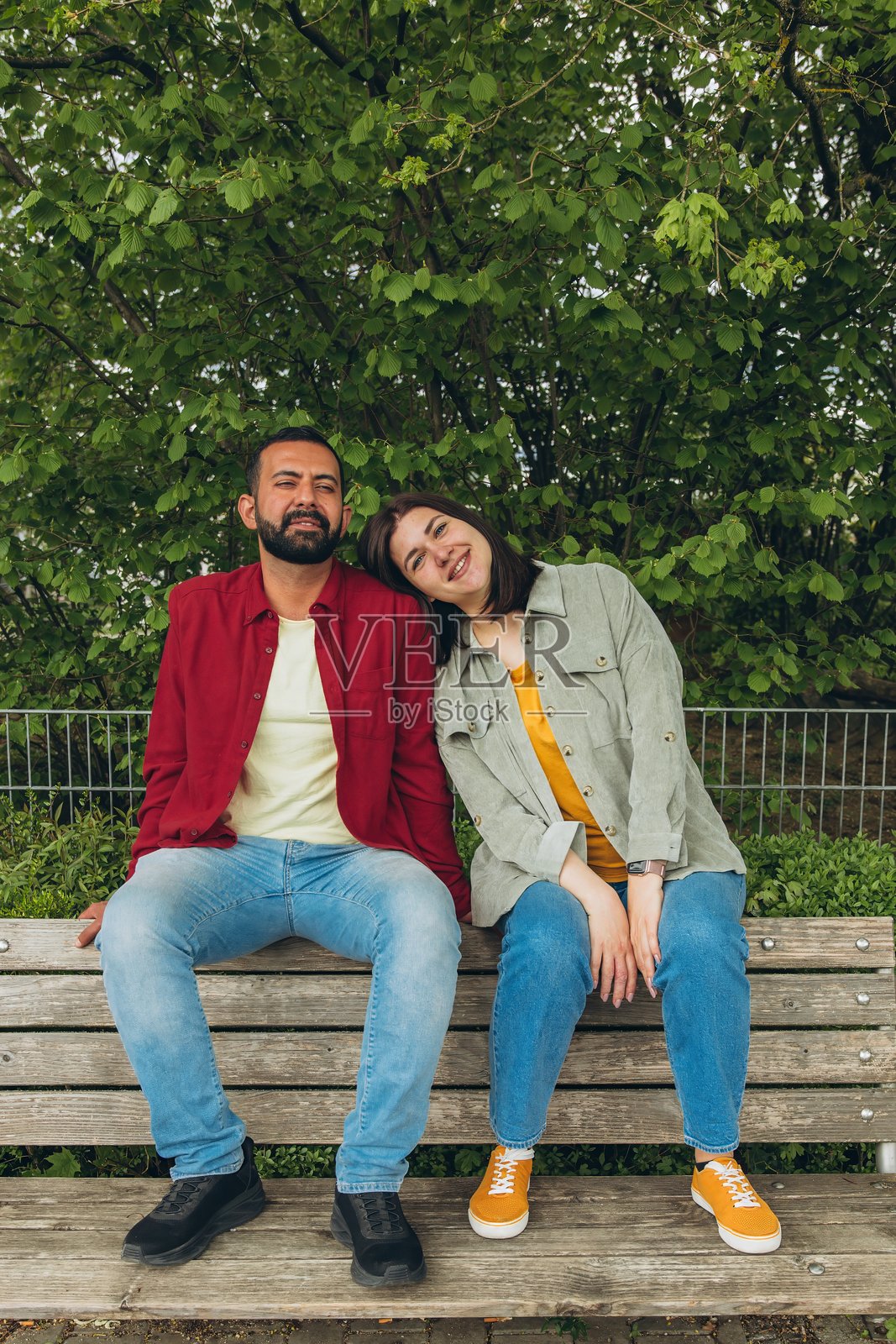 快乐的情侣坐在户外的长椅上,微笑着相拥在一起。这个愉快而亲密的时刻捕捉了爱情、联系和无忧无虑的相聚,展现了轻松自然的环境。照片摄影图片