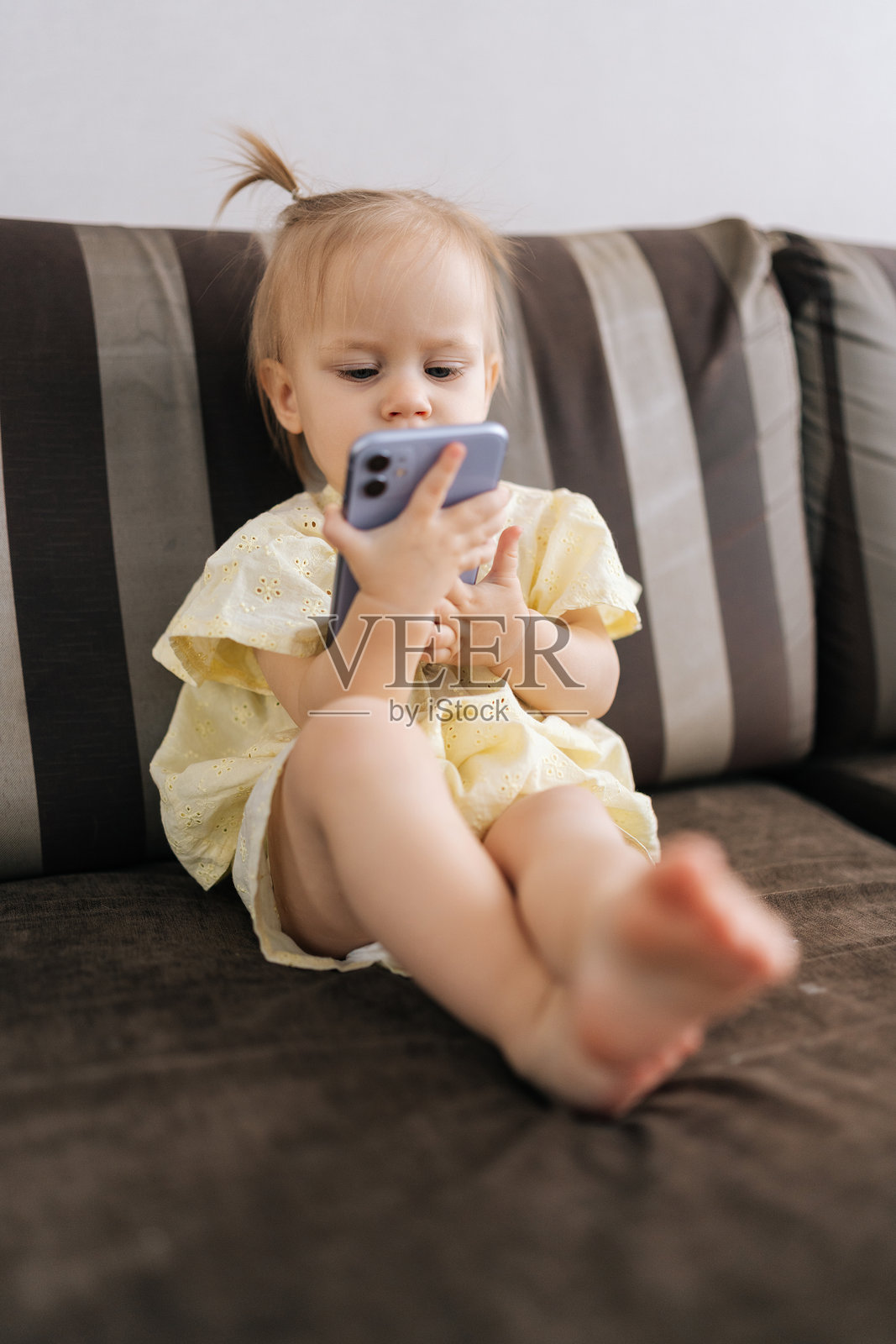 专注的幼儿女孩在家中舒适地坐着,使用智能手机屏幕探索数字内容的竖拍照片照片摄影图片