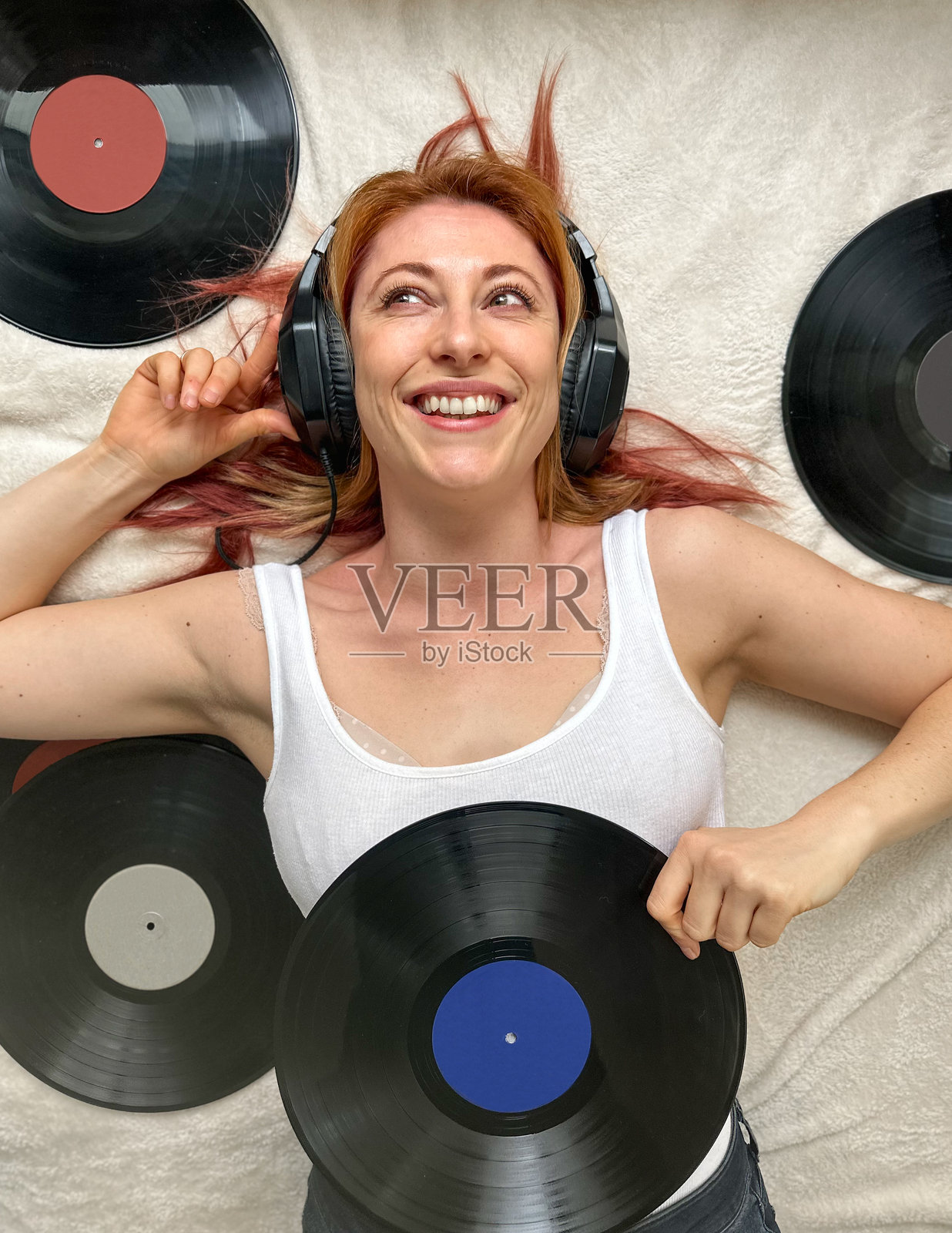 30多岁的女性,穿着舒适的家居服,躺在床上,戴着耳机听音乐。周围是复古的黑胶唱片。照片摄影图片