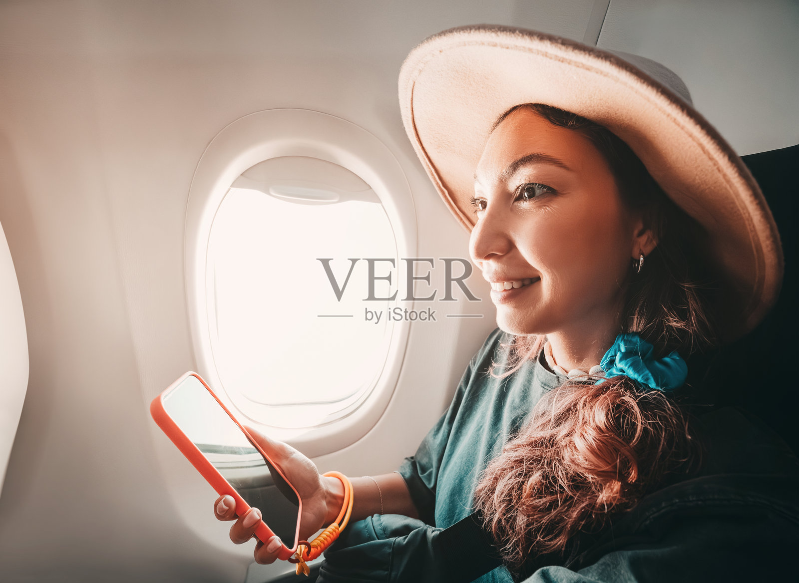 游客在飞行中享受使用智能手机的时光,透过窗户欣赏美丽的云朵和天空。照片摄影图片