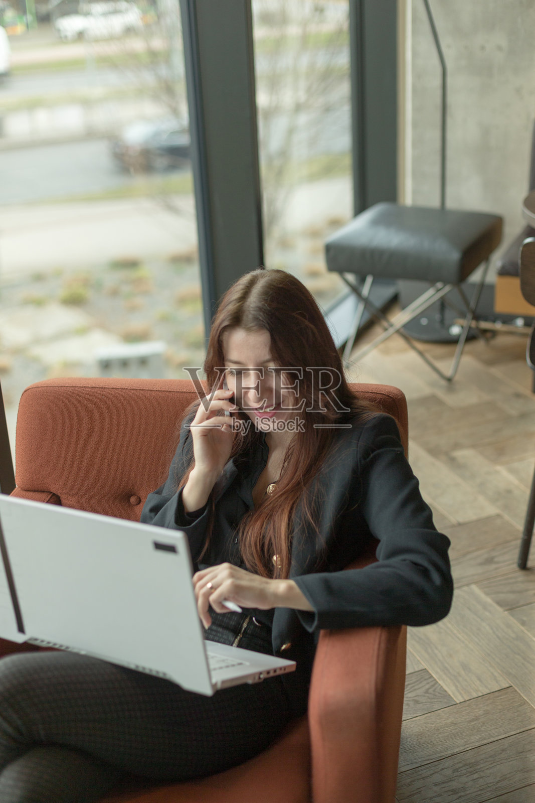 一位女性坐在椅子上使用笔记本电脑并打电话。照片摄影图片