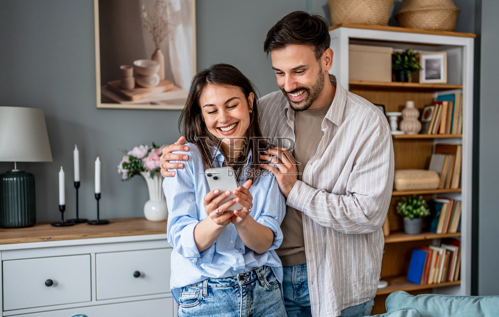 年轻情侣在家中使用智能手机时共享欢笑照片摄影图片