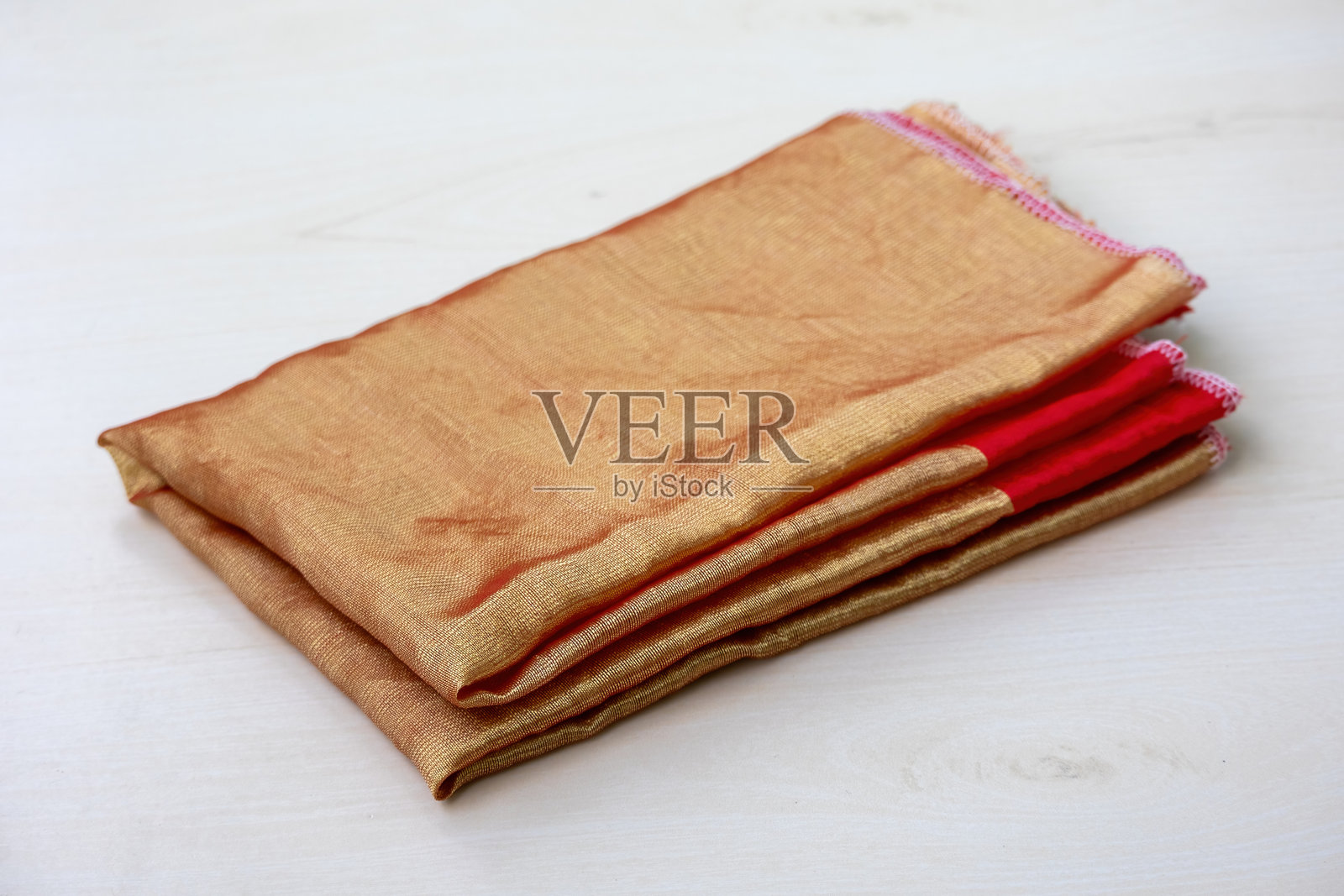 优雅的金色半丝棉织物,柔和地折叠在浅色木质背景上。非常适合纺织、时尚和手工艺项目。高质量的质感。照片摄影图片