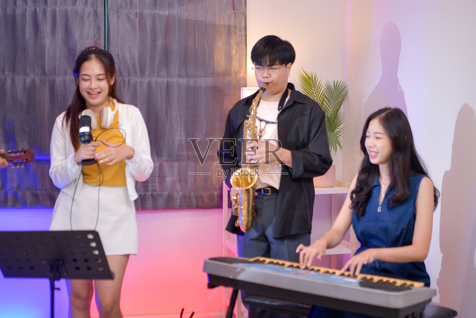年轻的亚洲乐队在室内演奏音乐,乐器包括吉他、键盘、萨克斯风和人声照片摄影图片