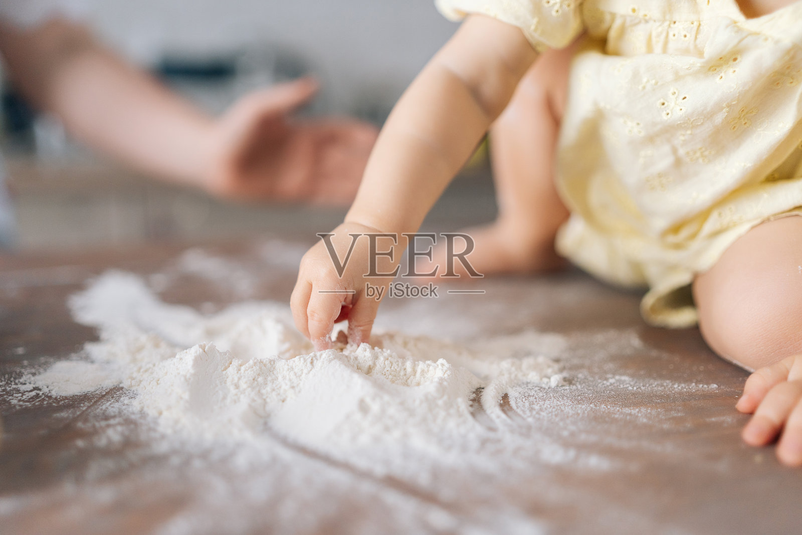 特写镜头,无法辨认的好奇幼儿女孩在桌子上顽皮地撒面粉,捕捉童年探索的快乐时刻。照片摄影图片