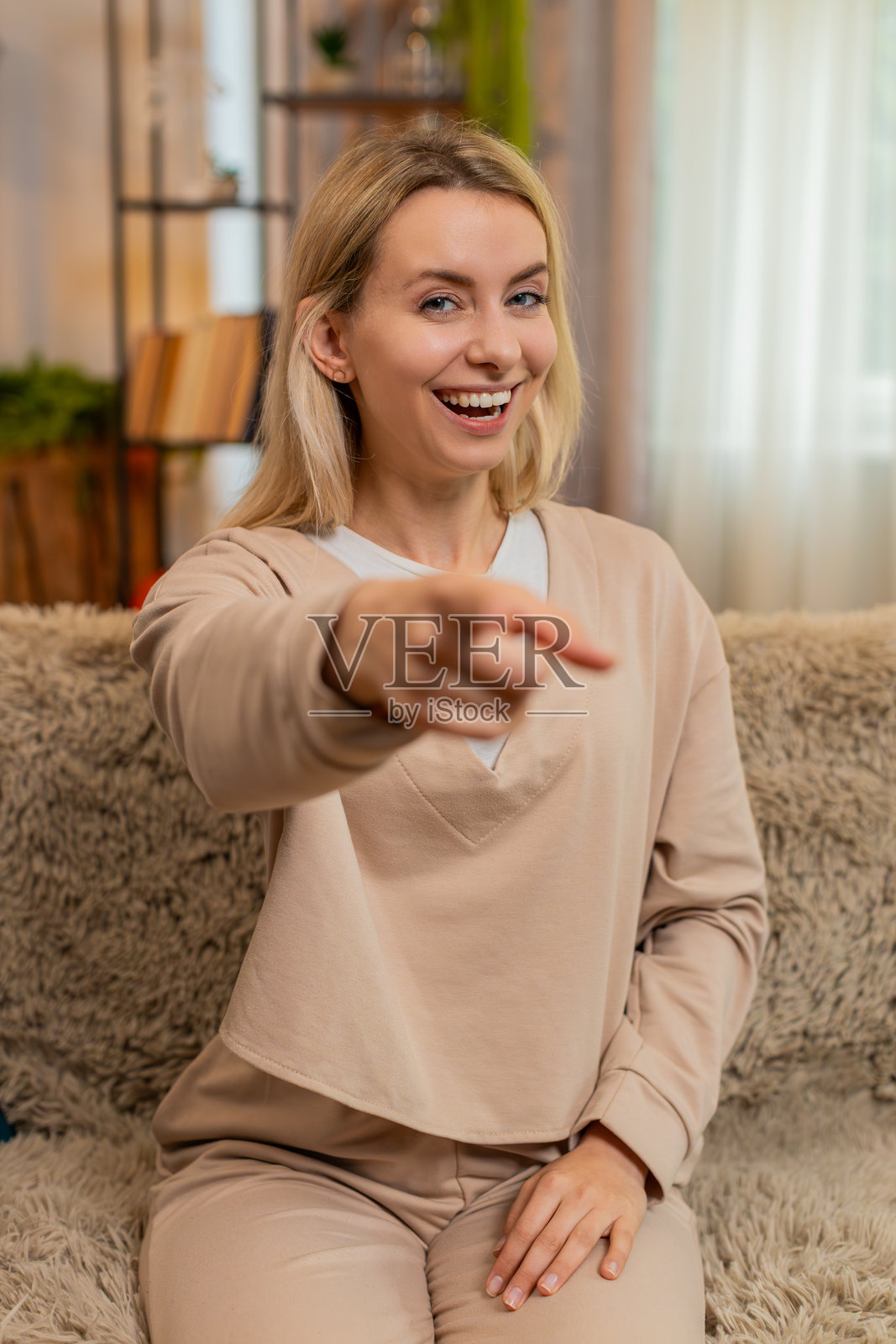 成年女性在家中指着相机,挥手微笑,充满快乐的能量,调皮地打招呼。照片摄影图片