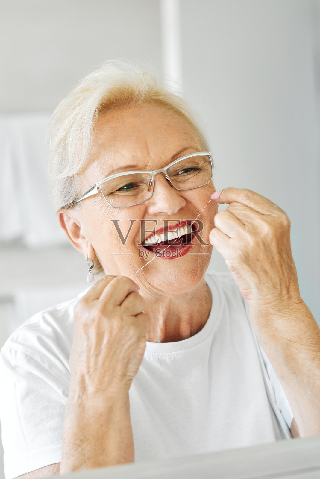 老年女性在浴室进行口腔卫生晨间护理,使用牙线和牙刷,保持口腔健康。照片摄影图片