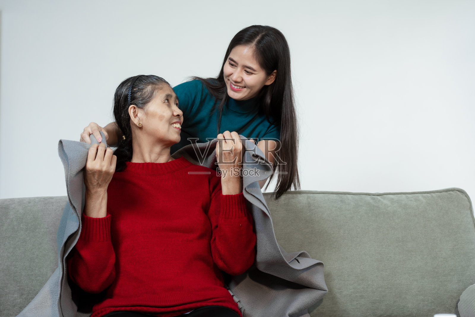 一位年轻的亚洲女性在家中细心照顾生病的母亲,坐在沙发上,提供药物和水,给予关怀的支持和细致的照料,营造出一个宁静的客厅环境。照片摄影图片