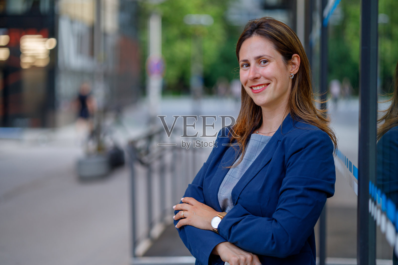 自信的女商人微笑着,双臂交叉,展现出专业风范,身处充满活力的城市环境中,体现成功与领导力。照片摄影图片