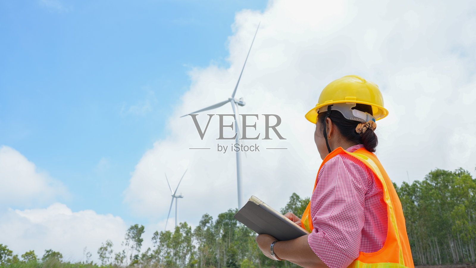 戴着安全帽和安全背心的女性在可再生能源领域观察风力涡轮机,展示了她对可持续实践和环境意识的承诺。照片摄影图片
