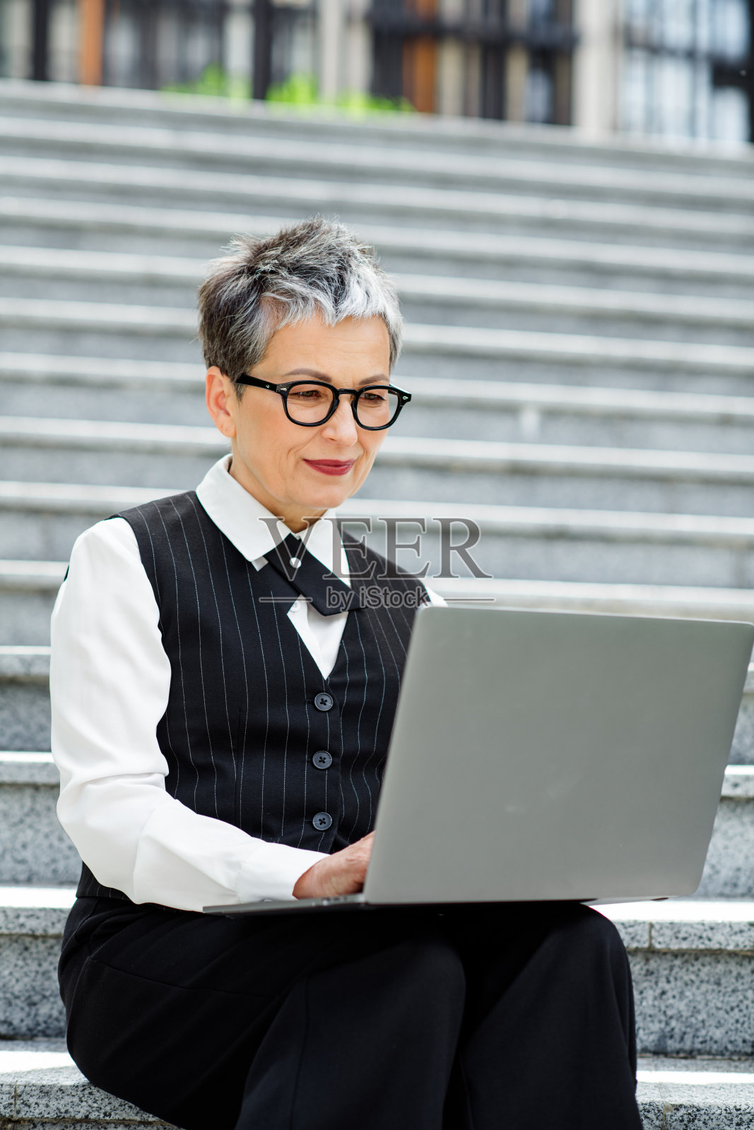 优雅的职业女性在户外使用笔记本电脑,展现出优雅和企业风格,背景为城市环境。照片摄影图片