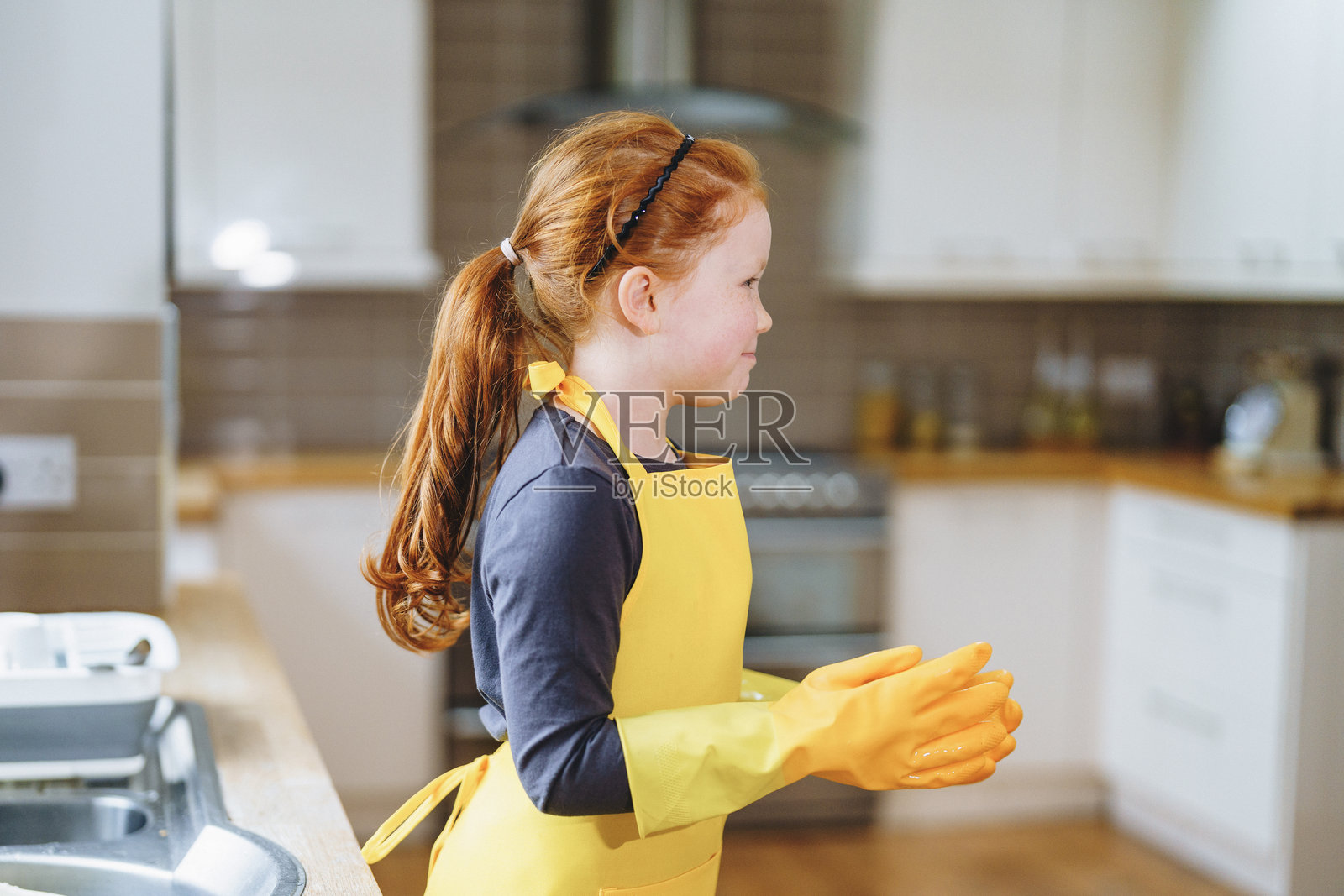 穿着黄色围裙和手套的孩子在明亮的厨房里准备帮助清洁,正值白天。照片摄影图片