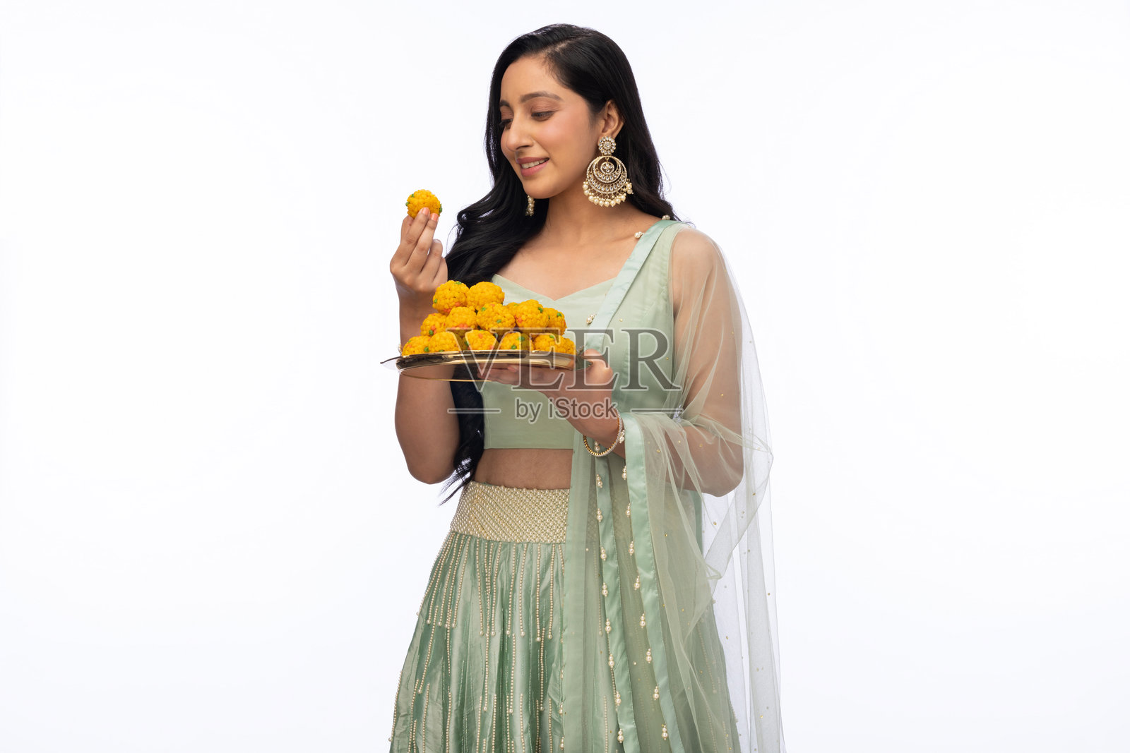 美丽女性在排灯节庆祝中手持拉杜,穿着传统服装,背景为白色。照片摄影图片