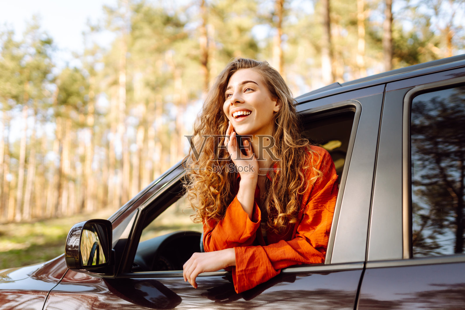 一位年轻女性在车窗旁欣赏日落,卷发随风飘扬。照片摄影图片