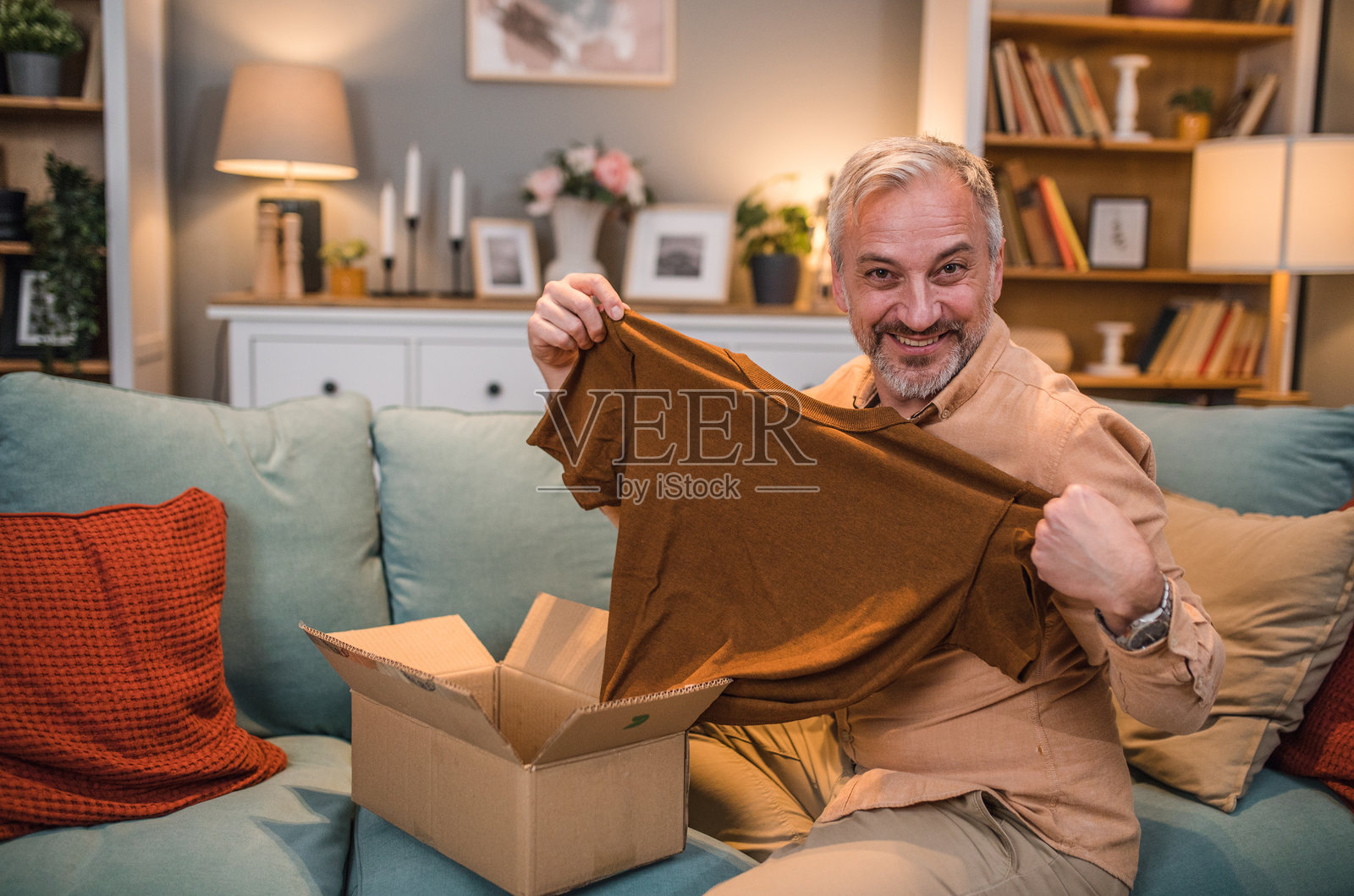 一位微笑的男子坐在客厅的沙发上拆开他在线订购的包裹照片摄影图片